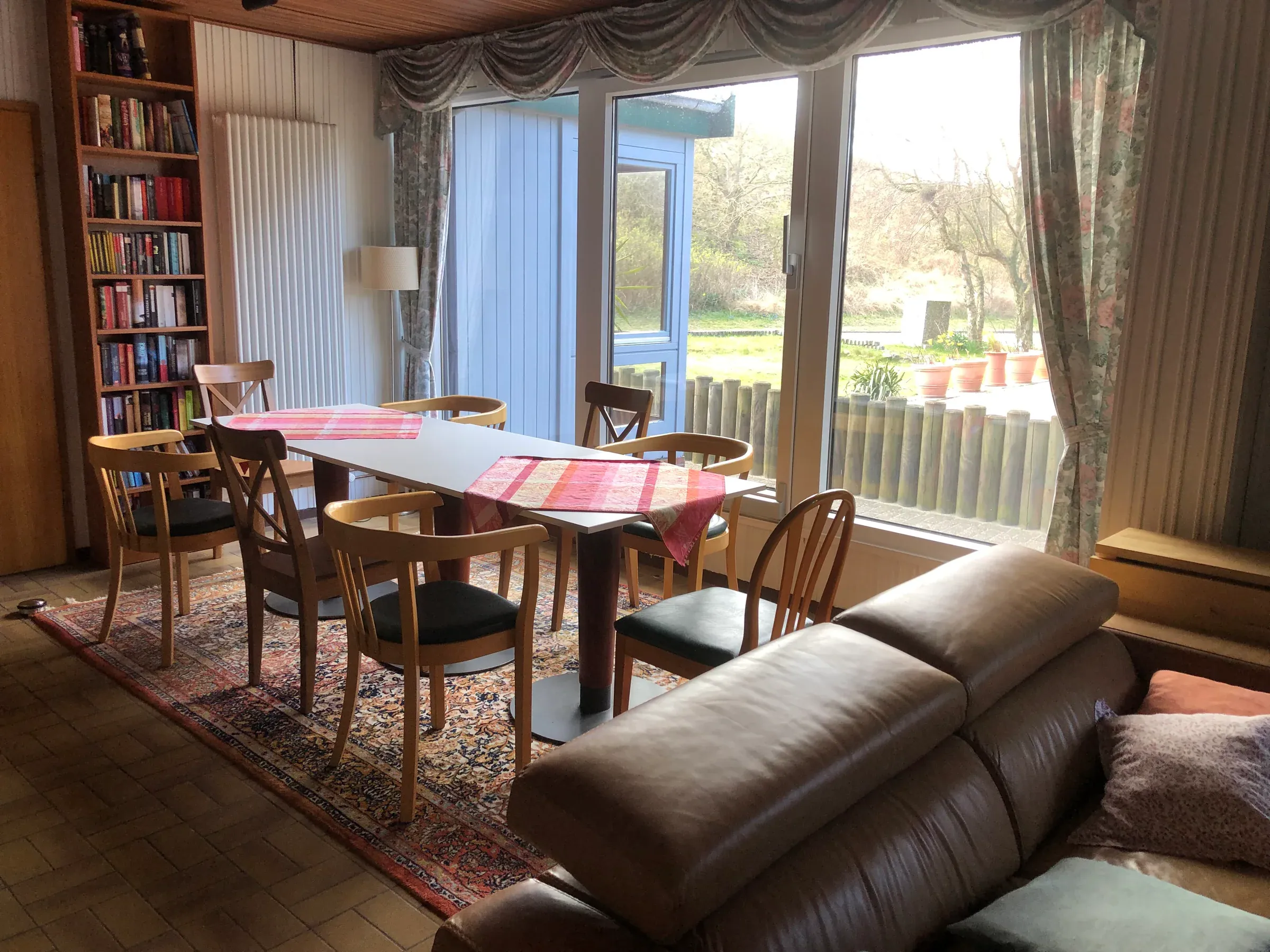Aufenthaltsraum im Haus Hertha mit Esstischen, Büchern und Blick ins Grüne